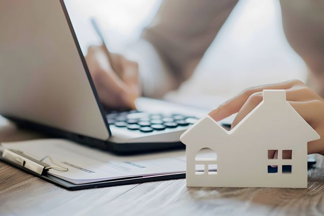 Foto: Person bearbeitet Akten, Modell eines Hauses im Vordergrund